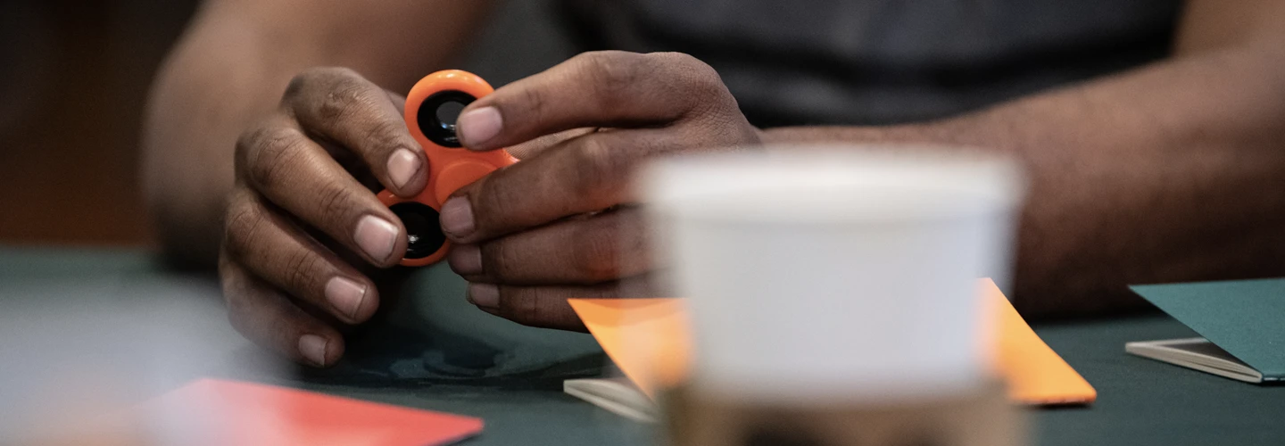 close-up of Black person's hands manipulating a fidget spinner device with notebooks on the table in front of them