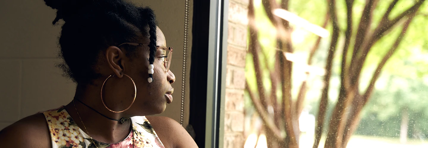 Young Black woman gazing out a window with a serious expression.