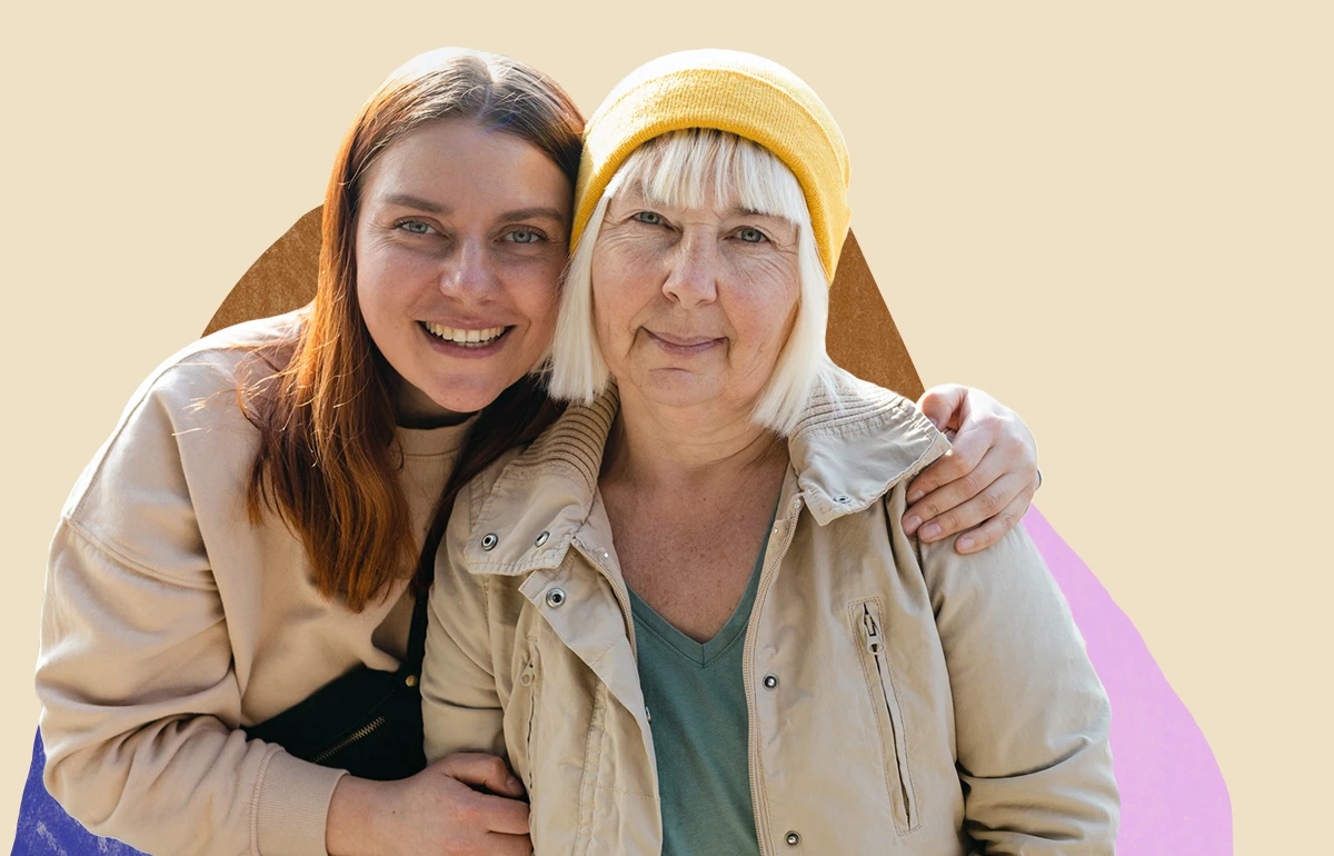 Young white woman hugging older white woman wearing a yellow cap. Both are smiling.