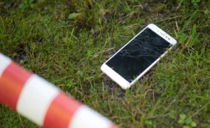 Cell phone with cracked screen lying in grass with police safety tape in foreground