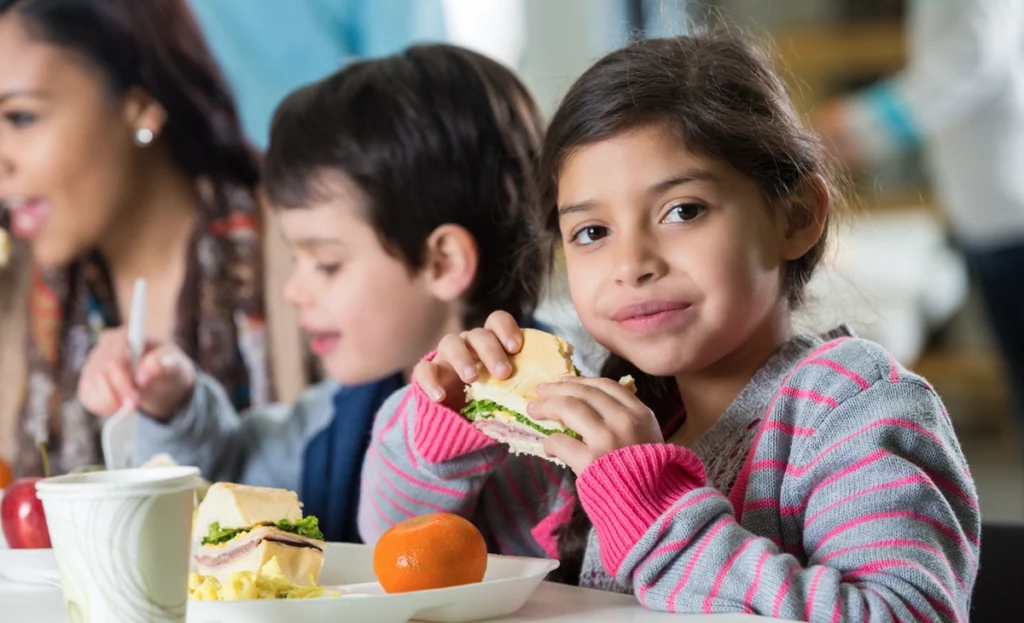 Children appear happy to eat a healthy lunch in a group setting.