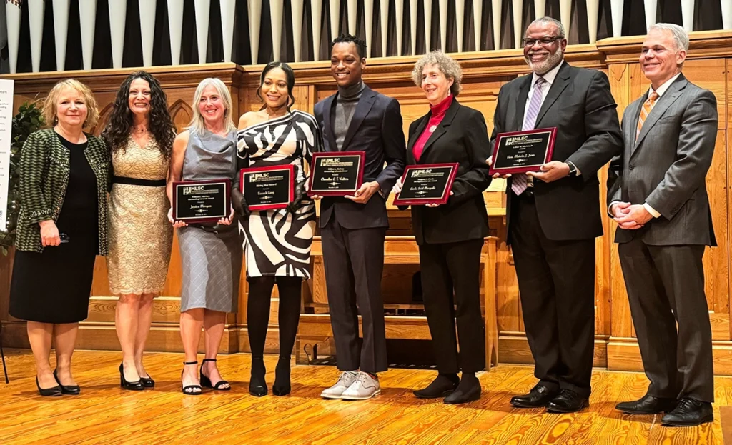 Eight people standing in a line holding award plaques.