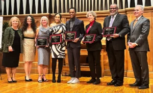 Eight people standing in a line holding award plaques.